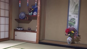 Una habitación japonesa tradicional con suelo de tatami, un panel shoji y una estantería con objetos decorativos.