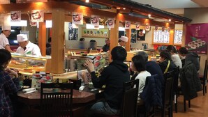 Un restaurante de sushi con interiores de madera y una barra donde los clientes hacen sus pedidos.