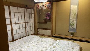 Una habitación japonesa tradicional con suelo de tatami, futón, puertas correderas shoji, un farol colgante y un rollo de caligrafía.