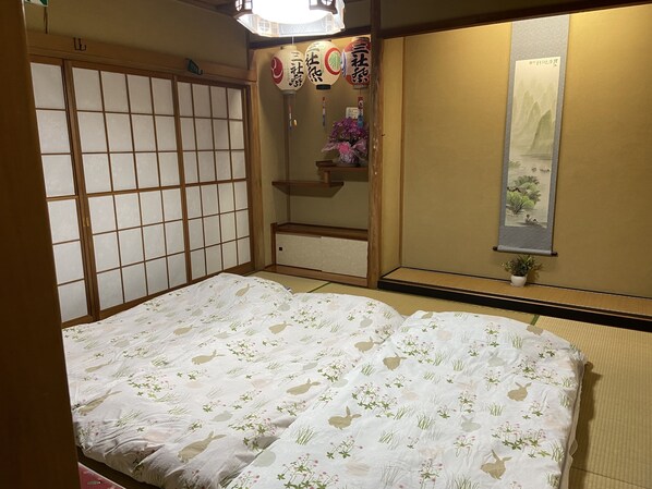 Perinteinen japanilainen huone, jossa on tatamimatto, futon-patja, liukuvat shoji-ovet, riippuvalaisin ja kalligrafiakirjoituksella koristeltu seinäkaide.