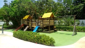 Un parque infantil con una casita de madera, toboganes y columpios.