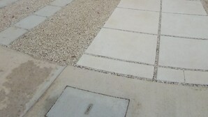 Un edificio moderno con techo plano, varias ventanas y un patio empedrado con grava y baldosas.