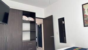 Un dormitorio con cama, armario, televisor y puerta.