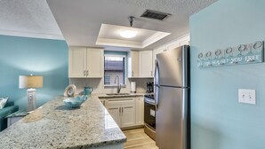 A modern kitchen with a granite countertop, stainless steel appliances, and light blue walls. - Emerald Isle 104 Beachfront|Updates Galore|Amazing SUNSET Views| 2 Bdrms (N. Redington Beach)