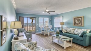 A living room with a ceiling fan, a sofa, a coffee table, and a dining area with chairs and a table. - Emerald Isle 104 Beachfront|Updates Galore|Amazing SUNSET Views| 2 Bdrms (N. Redington Beach)