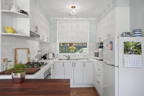 A modern kitchen with white cabinets, a wooden countertop, a stove, a sink, and a refrigerator.