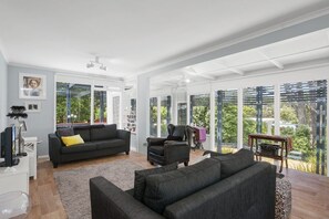 A spacious living room with a large window, a black sofa, a smaller armchair, and a coffee table.