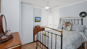 Quarto com cama, escrivaninha, cadeira, ventoinha no teto e janela com persianas.