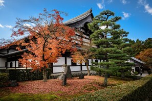 A traditional Japanese building with a tiled roof, surrounded by autumn foliage and a well-maintained garden.