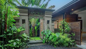 A tropical garden with a stone entrance, lush greenery, and a gravel pathway. - Charming Tropical Villa for Couple and Honeymooner (Gianyar)