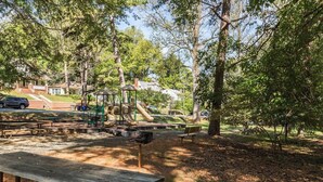 A park with picnic tables, playground equipment, and trees.