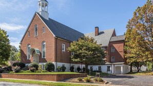 A large brick building with a prominent tower and arched windows, surrounded by trees and a well-maintained lawn.