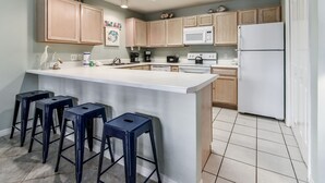 A modern kitchen with wooden cabinets, a white island with bar stools, and a white refrigerator. - Grand Caribbean East 111 * Fall Special Rates * Salt Water Vacations (Destin)