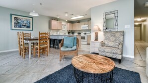 A spacious living room with a dining area, kitchen, and a patterned armchair. - Grand Caribbean East 111 * Fall Special Rates * Salt Water Vacations (Destin)