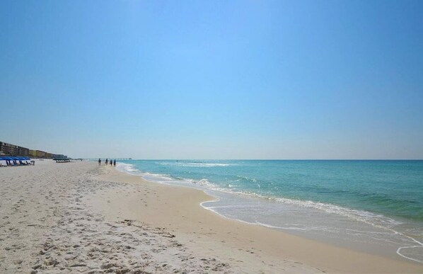A beach with a sandy shore, a pier in the distance, and a clear sky.