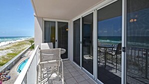 En balkon med pool, bord og stole, der udover en strand og et hav.