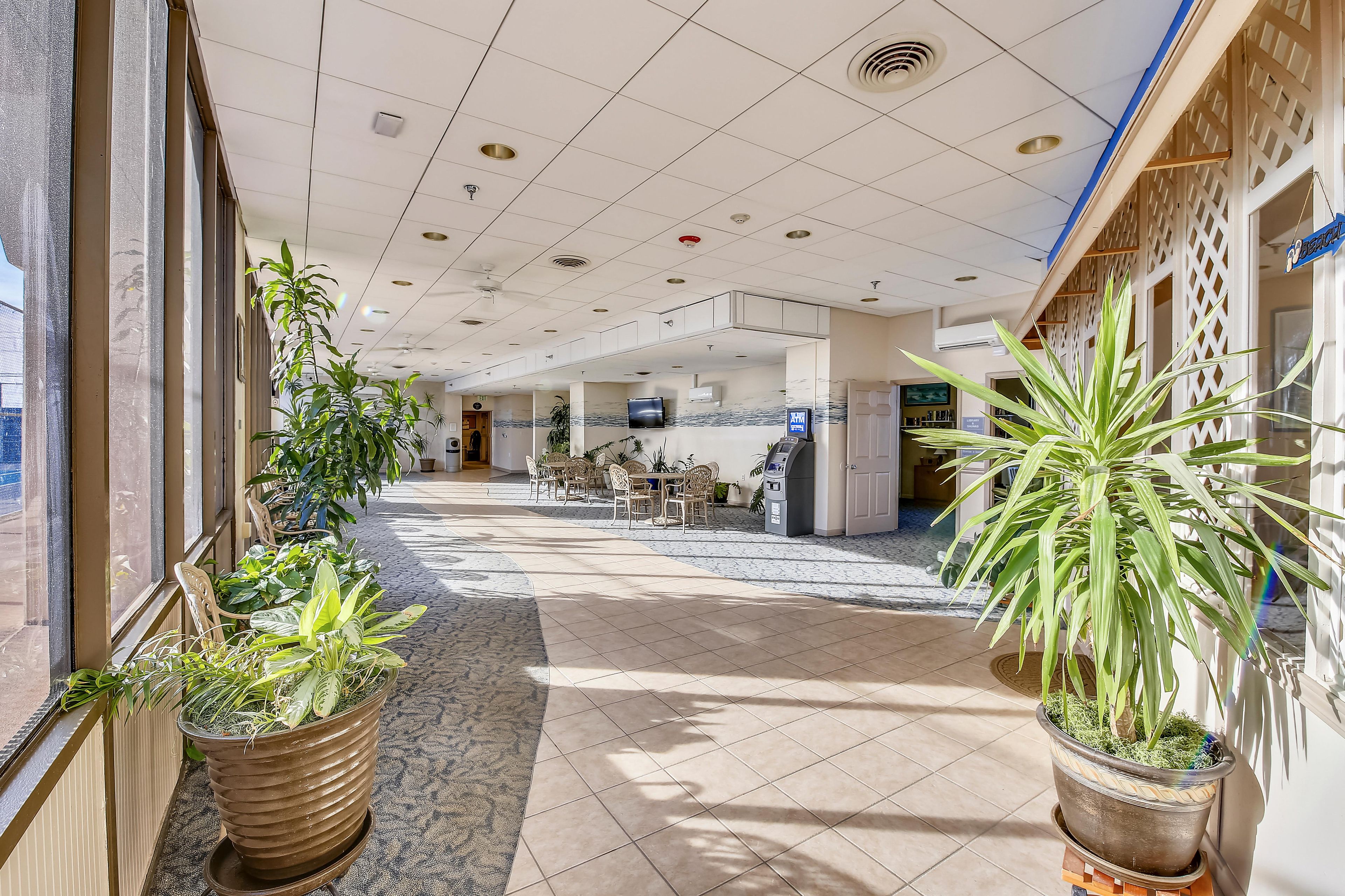 A hotel lobby with a tiled floor, potted plants, a reception desk, and a seating area.