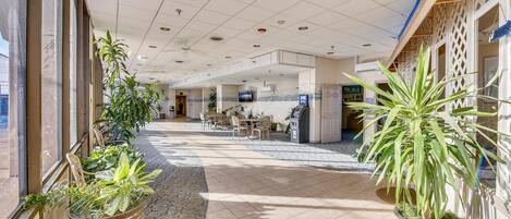 A hotel lobby with a tiled floor, potted plants, a reception desk, and a seating area.