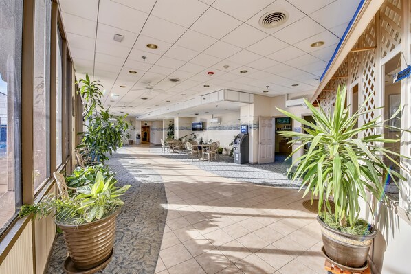 A hotel lobby with a tiled floor, potted plants, a reception desk, and a seating area.