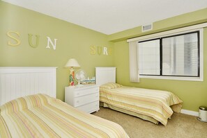 A bedroom with two beds, a dresser, a fan, and a window with curtains.