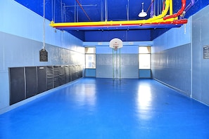 An indoor basketball court with a blue floor, a basketball hoop, and a 'NO DUNKING' sign.
