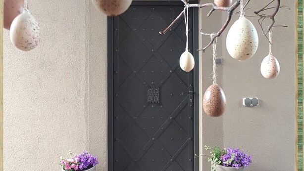 Une porte ornée d’œufs suspendus, avec deux plantes en pot de chaque côté.