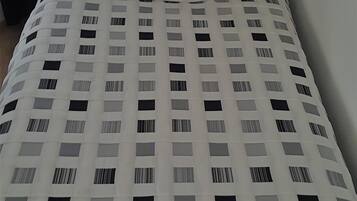 A bed with a white, grid-patterned mattress, a white pillow, and a white, fluffy blanket.