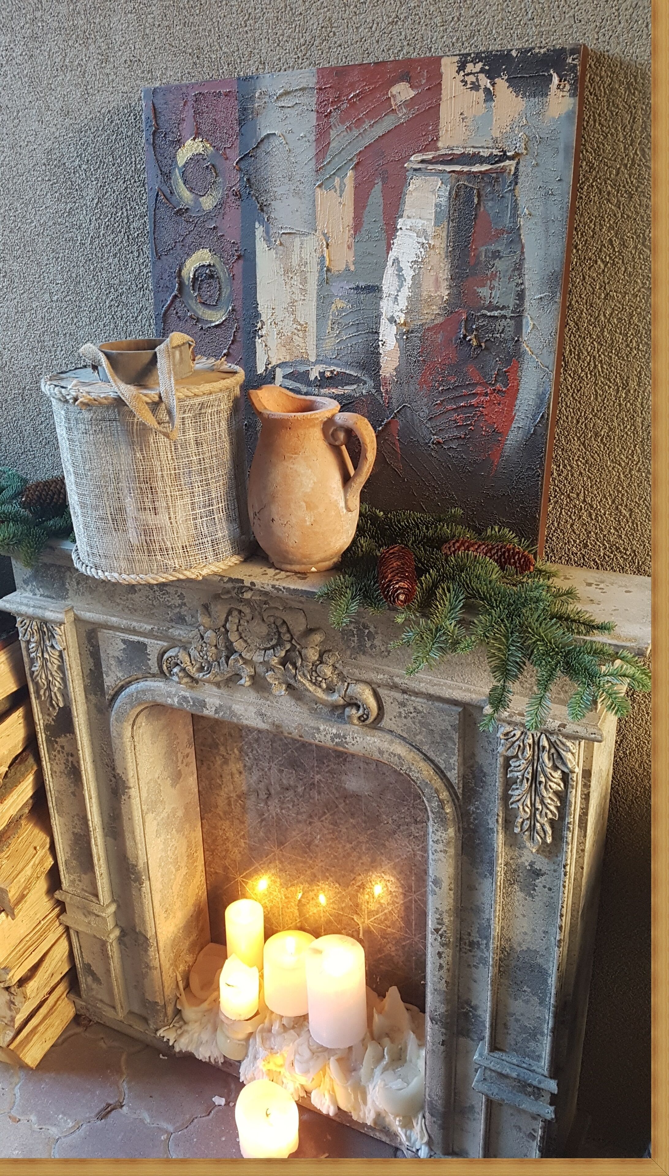 Ein Kamin mit drei brennenden Kerzen, rustischer Keramik und einem Bild an der Wand.