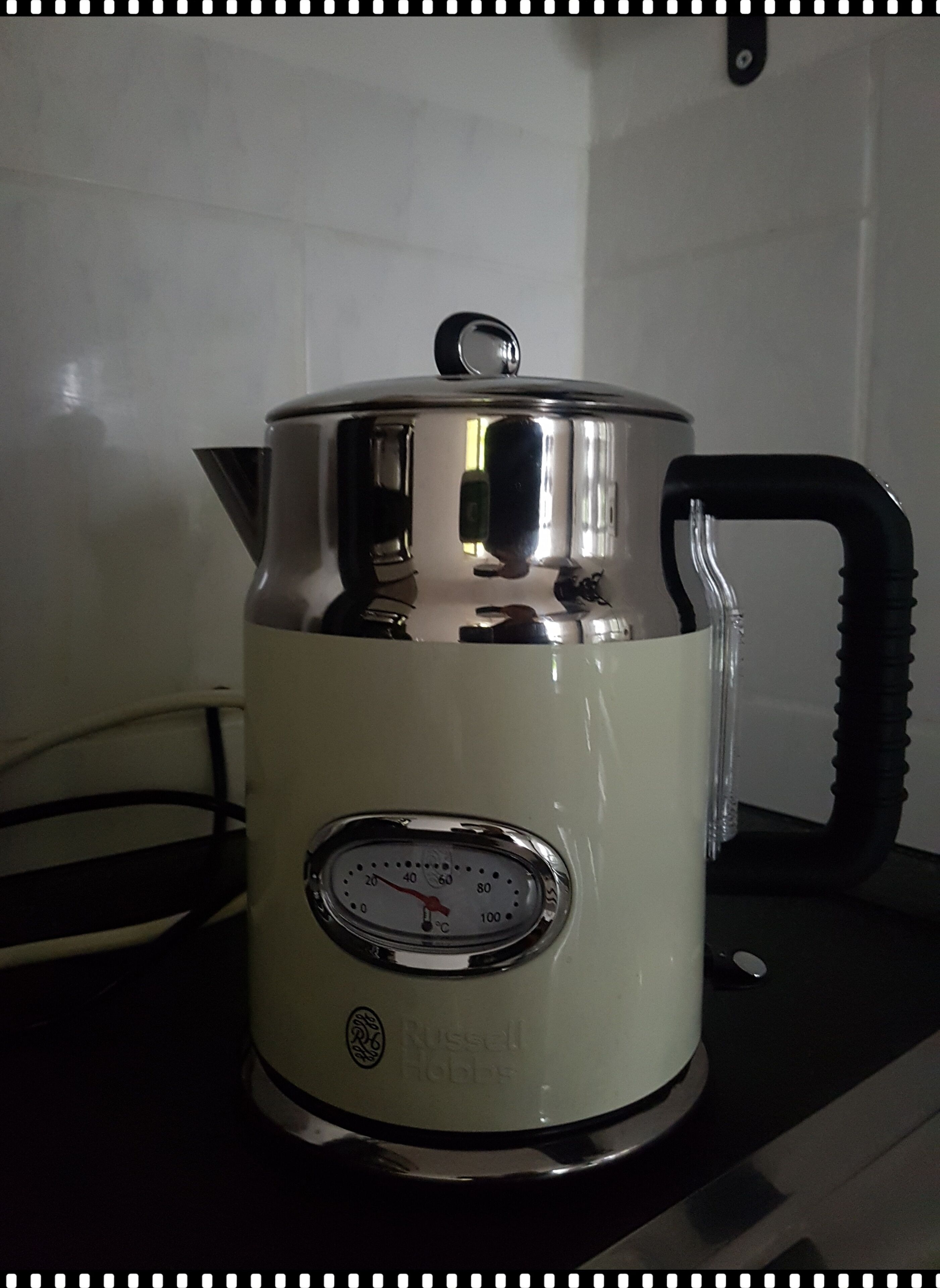Una tetera eléctrica Russell Hobbs blanca con indicador de temperatura digital y asa negra.