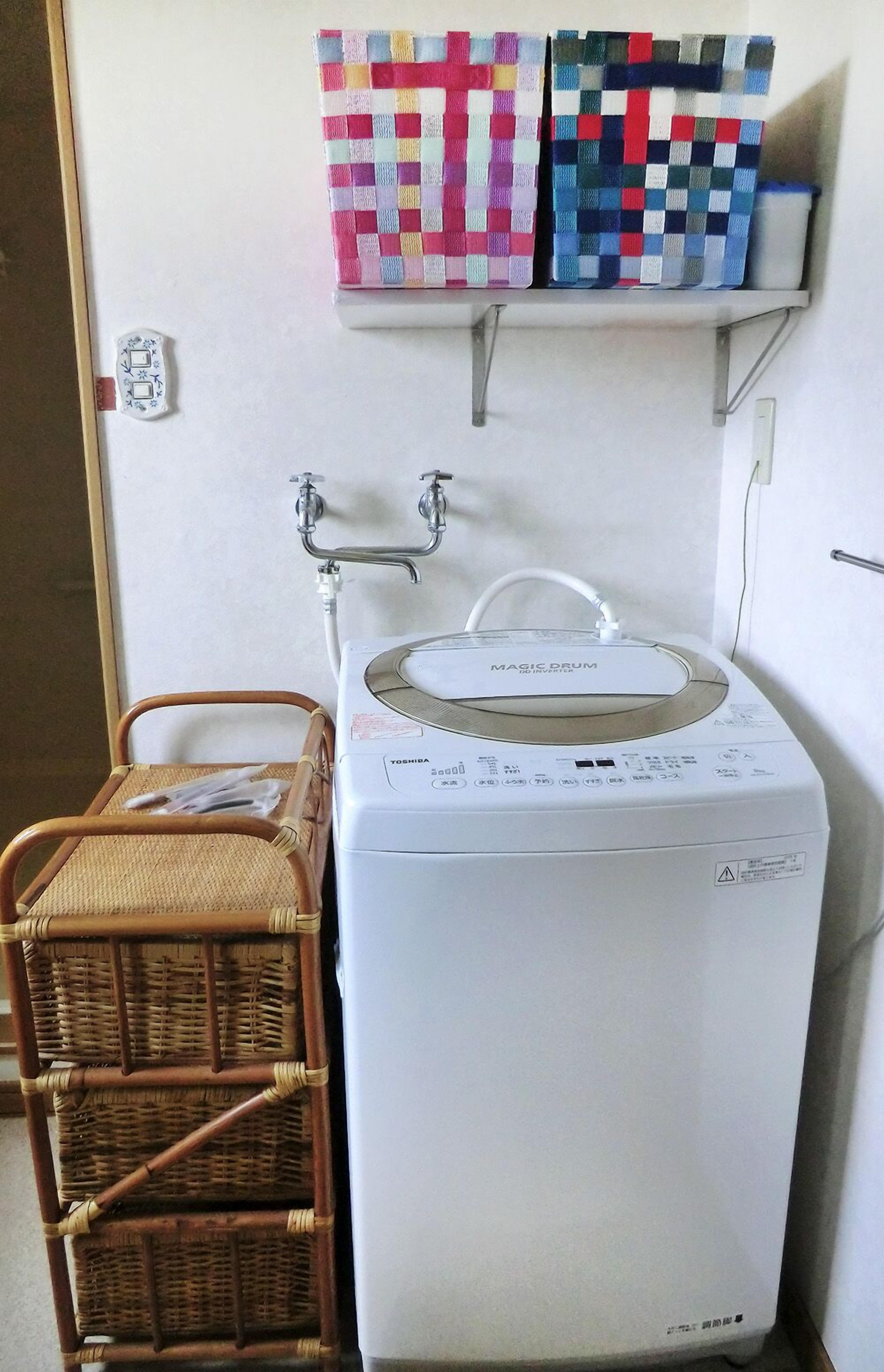 A washing machine with a control panel, a wicker basket, and a shelf with colorful storage boxes.
