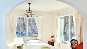 Une chambre à coucher avec un lit, une table de chevet, une chaise et une fenêtre donnant sur une forêt enneigée.