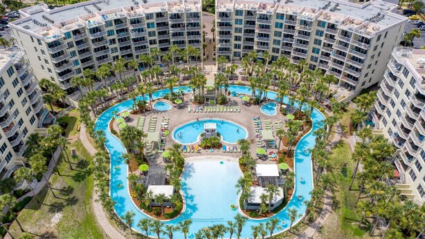 Un grande hotel con numerosi balconi, una piscina centrale e palme circostanti.