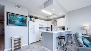 Una cucina moderna con mobili bianchi, un'isola centrale con sgabelli, un forno a microonde e una sveglia appesa al muro.
