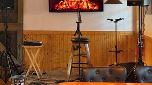 A room with a wooden ceiling, a fireplace, a television mounted on the wall, a dining table with chairs, and a microphone stand. - Lava Mountain Lodge (Dubois)