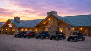 A log cabin with a stone chimney, a sign reading 'Thai Lodge,' and four off-road vehicles parked in front. - Lava Mountain Lodge (Dubois)