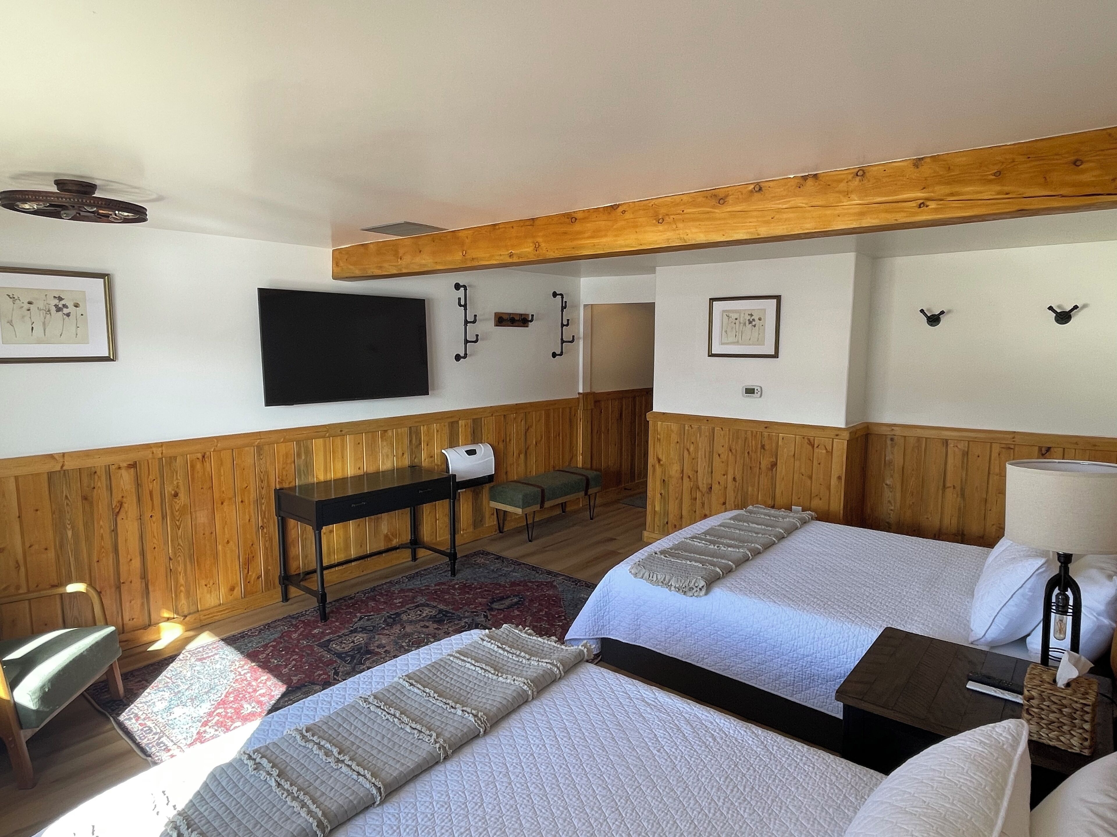 Ein Hotelzimmer mit zwei Betten, einem Schreibtisch, einem Stuhl, einem Fernseher und einer Holzbodenverkleidung.