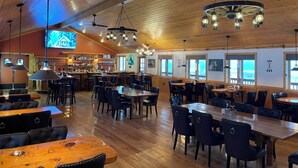A restaurant with wooden ceiling, multiple tables and chairs, a bar area, and large windows. - Lava Mountain Lodge (Dubois)