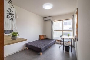 Una habitación pequeña y moderna con una cama individual, una mesita con una planta y una ventana con cortinas.