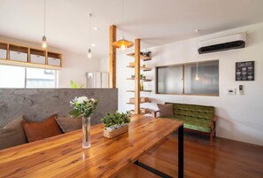 Ein modernes Interieur mit einem Holzes Esstisch, einem grünen Sofa und einem großen Fenster.