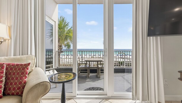 Une pièce comprenant un canapé, une petite table, un téléviseur et une porte-fenêtre coulissante donnant sur un balcon avec vue sur la plage.