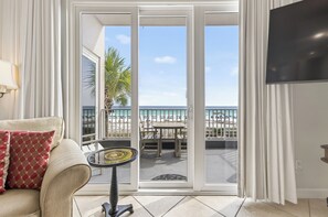 A room with a sofa, a small table, a TV, and a sliding glass door leading to a balcony with a beach view. - Inn at Crystal Beach 210 * Gulf Front with Beach Chair Set. Onsite dining! (Destin)
