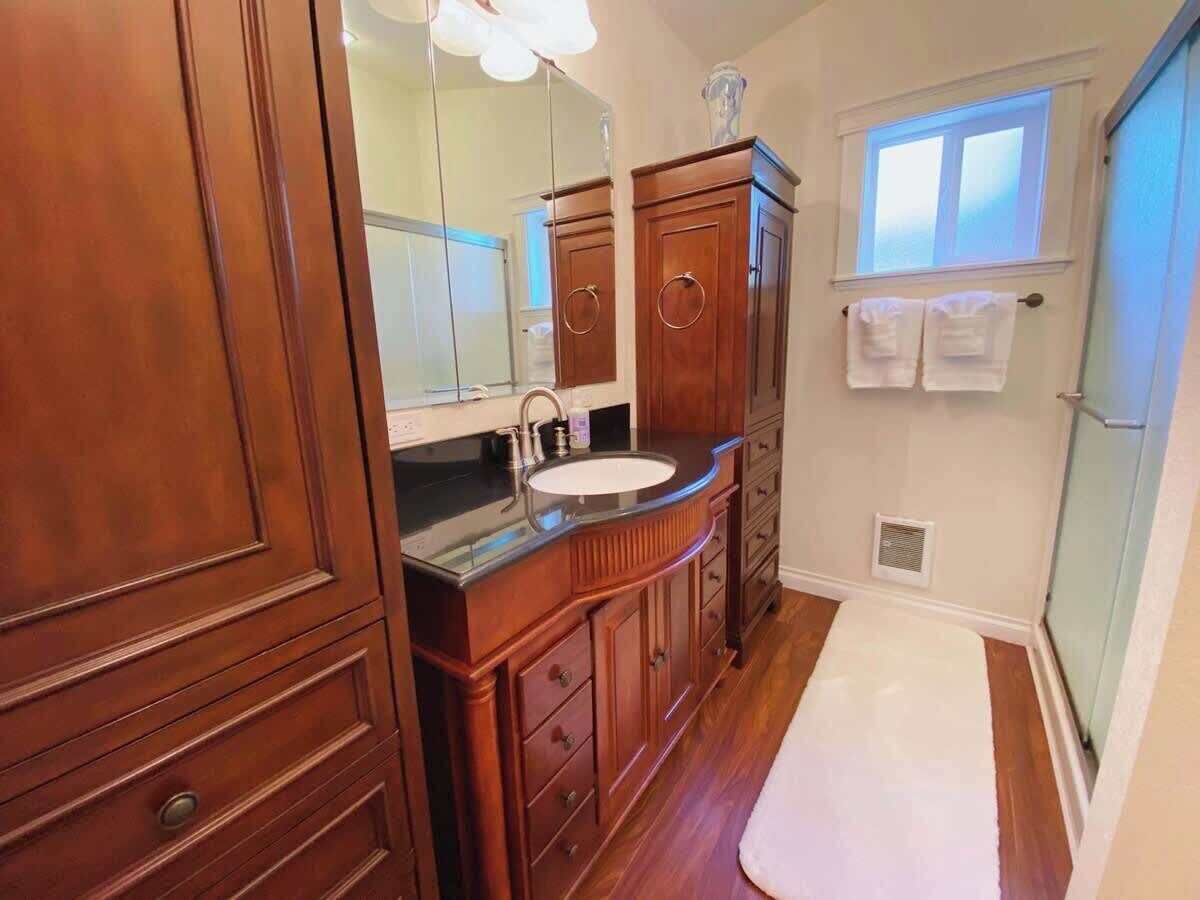 Een badkamer met houten kastjes, een wastafel, een spiegel en een raam.