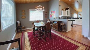 A dining area with a wooden ceiling, a chandelier, and a red patterned rug.