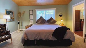 A bedroom with a large bed, a window, a lamp, and a chair.