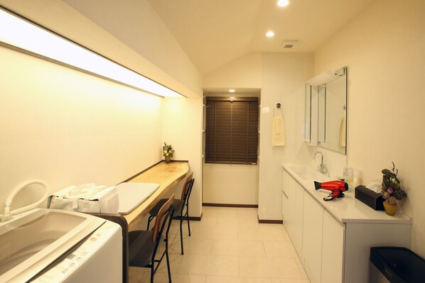 A compact hotel bathroom with a washing machine, a sink, a mirror, and a small table with a hairdryer. - -TOUCHIAN- Quiet Modern Villa Okayama (Okayama-shi)