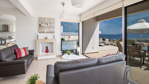 Un salon moderne avec un canapé, une table basse et une cheminée. Il y a un balcon avec des sièges d’extérieur et une vue sur la mer.
