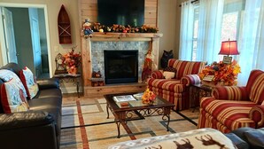 Ein gemütliches Wohnzimmer mit Kamin, gestreiften Sesseln, einer Couch und einem Couchtisch.