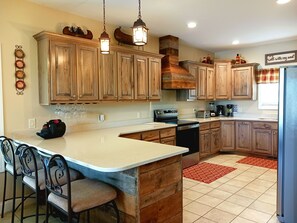 A kitchen with wooden cabinets, a central island with bar stools, a stove, and a refrigerator. - LAKEFRONT 4/3.5, Private Dock, Pool Table, Lakeside Firepit, Kayaks, Paddleboat (Young Harris)