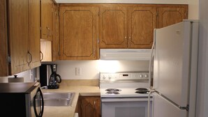 A compact kitchen with wooden cabinets, a microwave, a stove, and a refrigerator. - Corner Midtown Apartment (Anchorage)