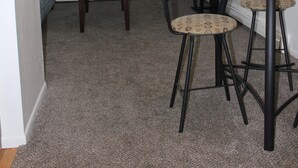 A small dining area with a glass table and four chairs, a television on a stand, a window with a view of a house, and a door leading to another room. - Corner Midtown Apartment (Anchorage)
